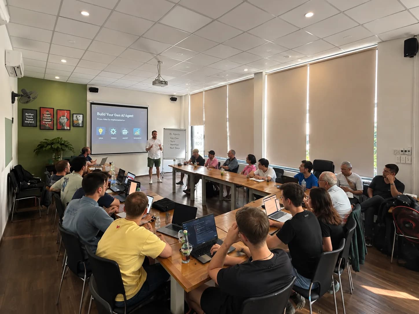 KI-Workshop in einem Seminarraum in Danang: rund zwanzig Teilnehmer mit Laptops an Tischen, vorn präsentiert ein Referent die Folie Build Your Own AI Agent
